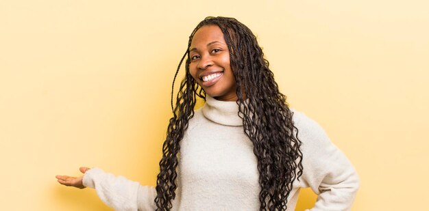 Mujer bonita negra que se siente feliz y alegre sonriendo y dándote la bienvenida invitándote a entrar con un gesto amistoso