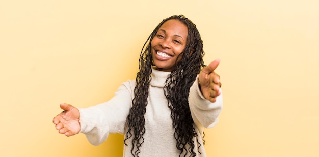 Mujer bonita negra sonriendo alegremente dando un cálido abrazo de bienvenida cariñoso sintiéndose feliz y adorable