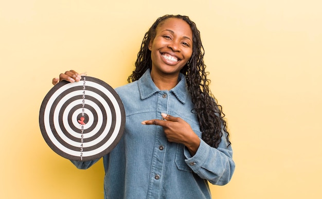 Mujer bonita negra sonriendo alegremente sintiéndose feliz y apuntando hacia un lado