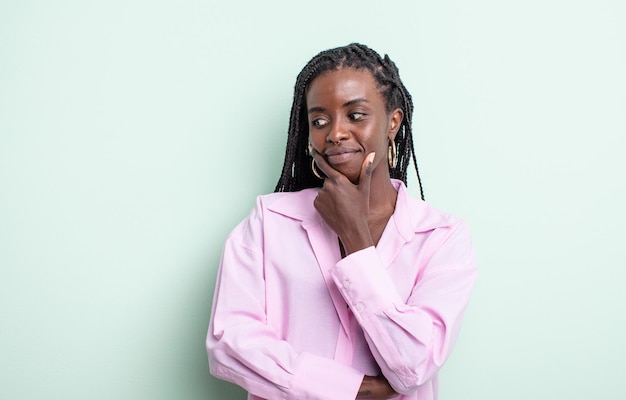 Mujer bonita negra sonriendo con una expresión feliz y segura con la mano en la barbilla, preguntándose y mirando hacia un lado