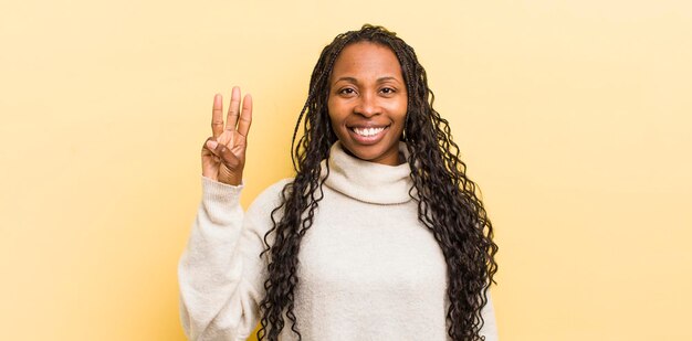 Mujer bonita negra sonriendo y luciendo amigable mostrando el número tres o tercero con la mano hacia adelante contando hacia atrás