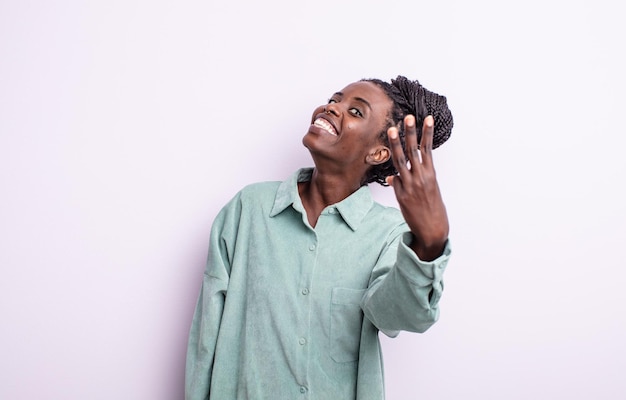 Mujer bonita negra sonriendo y mirando amistosamente, mostrando el número tres o tercero con la mano hacia adelante, contando hacia atrás