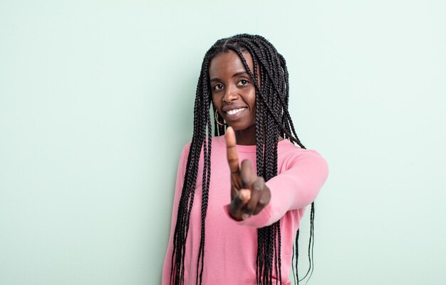 Mujer bonita negra sonriendo con orgullo y confianza haciendo la pose número uno triunfalmente, sintiéndose como una líder