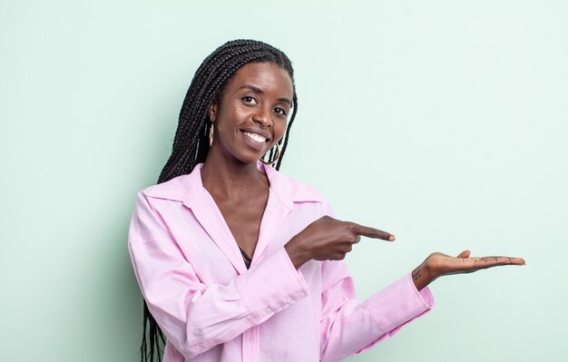 Mujer bonita negra sonriendo, sintiéndose feliz, despreocupada y satisfecha, señalando el concepto o la idea en el espacio de la copia en el lateral