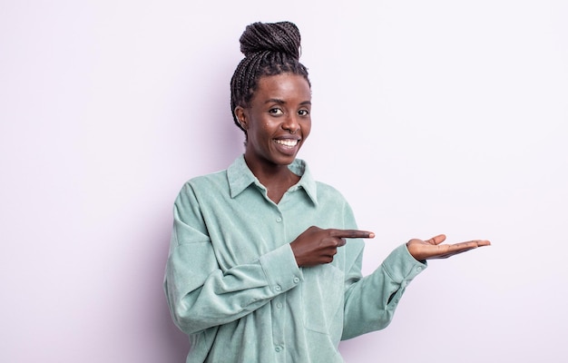 Mujer bonita negra sonriendo, sintiéndose feliz, despreocupada y satisfecha, señalando el concepto o la idea en el espacio de la copia en el lateral