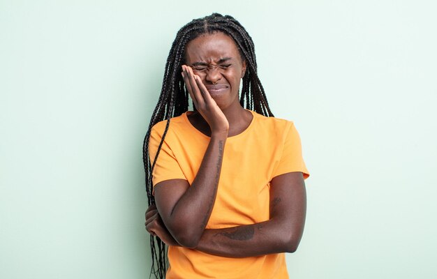 Mujer bonita negra sosteniendo la mejilla y sufriendo dolor de muelas, sintiéndose enferma, miserable e infeliz, buscando un dentista