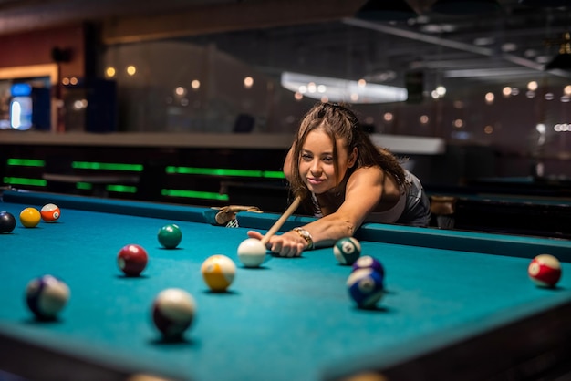 Una mujer bonita pasa tiempo libre jugando al billar en el pub