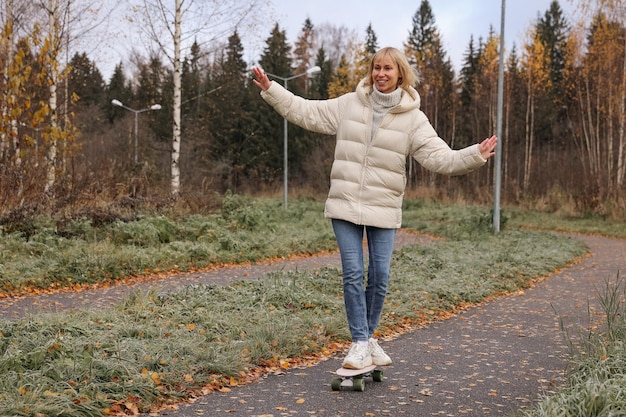 Una mujer bonita patinando en un parque de otoño, aprendiendo a patinar en patineta pasando el fin de semana al aire libre. Concepto de deporte saludable.