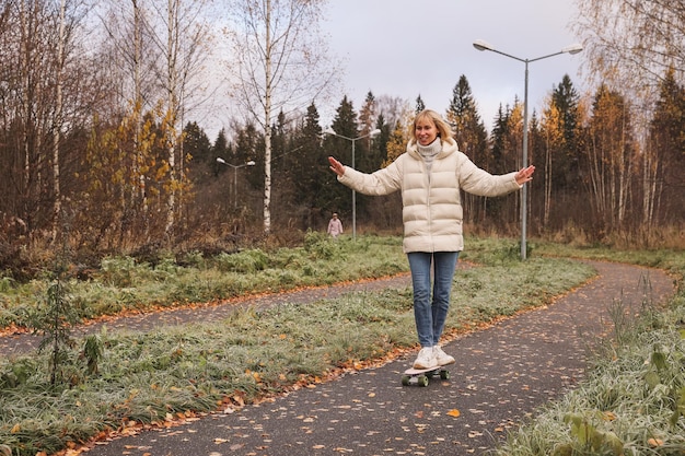 Una mujer bonita patinando en un parque de otoño, aprendiendo a patinar en patineta pasando el fin de semana al aire libre. Concepto de deporte saludable.