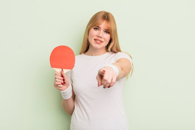 Mujer bonita pelirroja apuntando a la cámara eligiendo tu concepto de ping pong