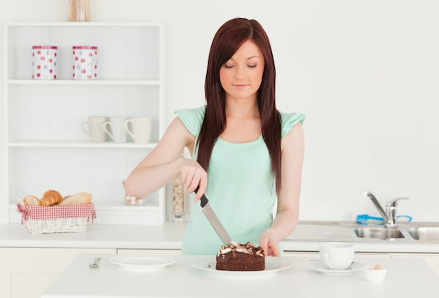 Foto mujer bonita pelirroja cortando pastel en la cocina