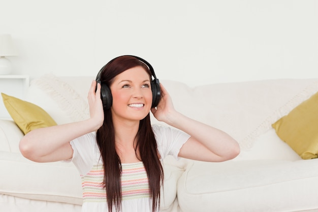 Mujer bonita pelirroja escuchando música con auriculares mientras está sentado en una alfombra