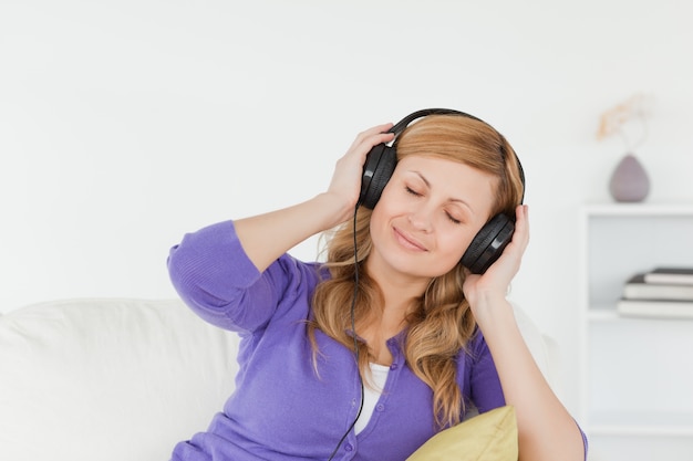 Mujer bonita pelirroja escuchando música y disfrutando el momento mientras está sentado en un sofá