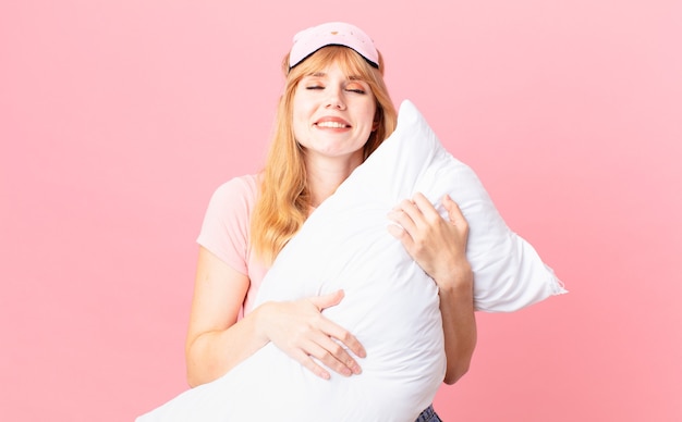 Mujer bonita pelirroja en pijama y sosteniendo una almohada