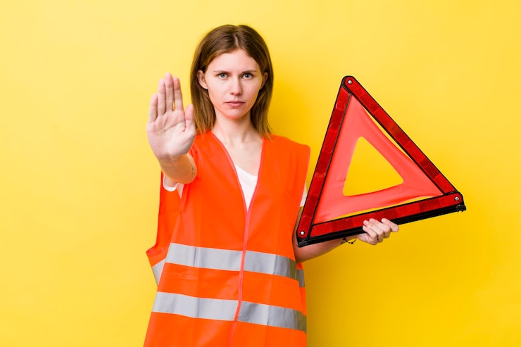 Foto mujer bonita pelirroja que parece seria mostrando la palma abierta haciendo un gesto de parada coche triangre peligro