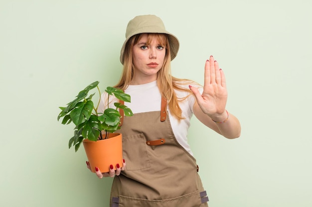 Mujer bonita pelirroja que parece seria mostrando la palma abierta haciendo un gesto de parada concepto de jardinero