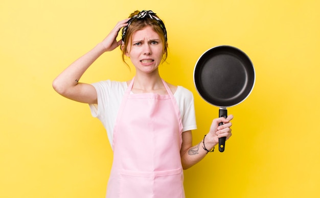 Mujer bonita pelirroja que se siente estresada, ansiosa o asustada con las manos en la cabeza, sartén y concepto de ama de casa