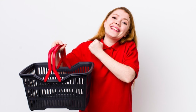 Mujer bonita pelirroja que se siente feliz y se enfrenta a un desafío o celebra el concepto de cesta de la compra vacía