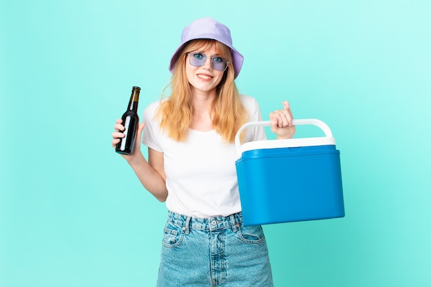 Mujer bonita pelirroja con un refrigerador portátil y una cerveza