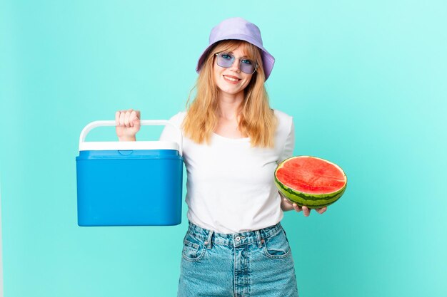 Mujer bonita pelirroja con un refrigerador portátil y una sandía