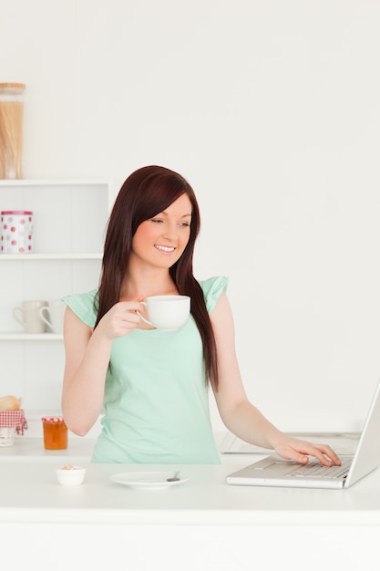 Mujer bonita pelirroja relajante con su computadora portátil en la cocina