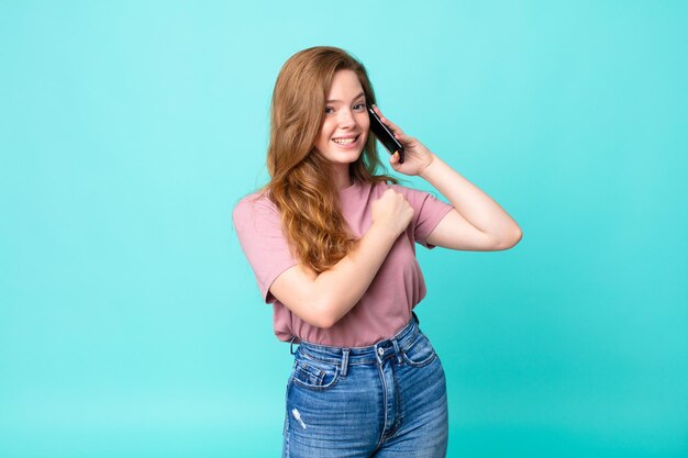 Mujer bonita pelirroja sintiéndose feliz y enfrentando un desafío o celebrando y usando un teléfono inteligente