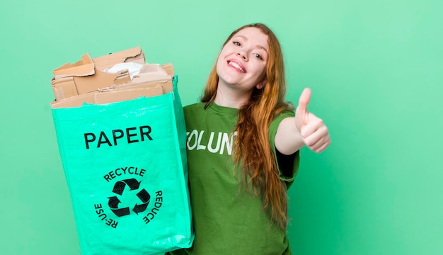 Mujer bonita pelirroja sintiéndose orgullosa sonriendo positivamente con los pulgares hacia arriba concepto de reciclaje