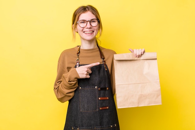 Mujer bonita pelirroja sonriendo alegremente sintiéndose feliz y señalando el concepto de entrega lateral para llevar