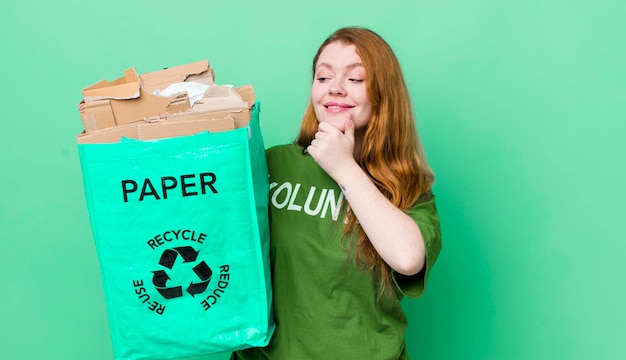 Mujer bonita pelirroja sonriendo con una expresión de confianza feliz con la mano en el concepto de reciclaje de la barbilla