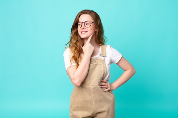 Mujer bonita pelirroja sonriendo felizmente y soñando despierto o dudando