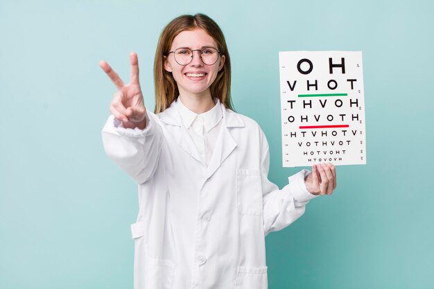 Mujer bonita pelirroja sonriendo y luciendo feliz gesticulando victoria o concepto de prueba de visión óptica de paz