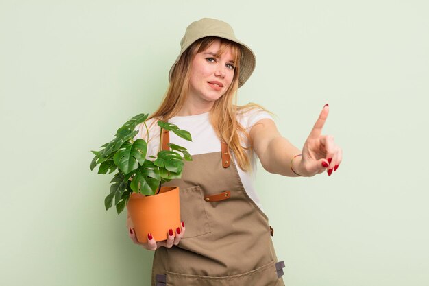 Mujer bonita pelirroja sonriendo con orgullo y confianza haciendo el número uno. concepto de jardinero