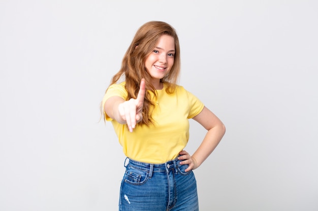 Mujer bonita pelirroja sonriendo con orgullo y confianza haciendo el número uno