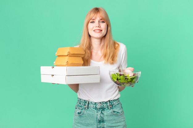 Mujer bonita pelirroja sosteniendo cajas de comida rápida y una ensalada