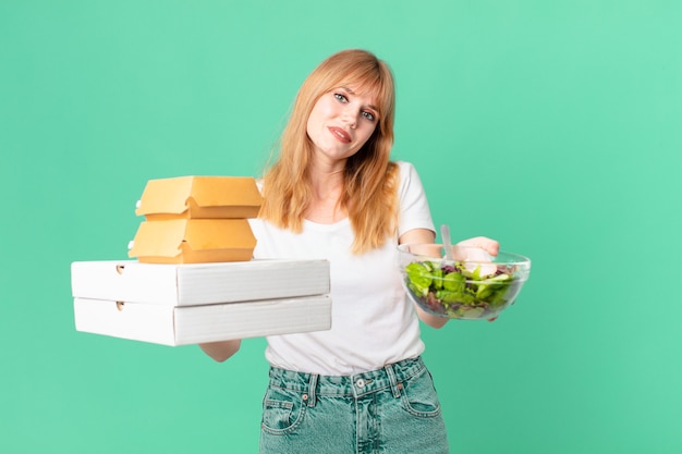 Mujer bonita pelirroja sosteniendo cajas de comida rápida y una ensalada