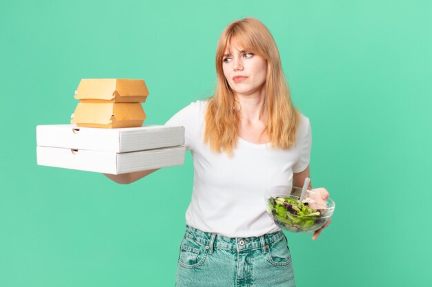 Mujer bonita pelirroja sosteniendo cajas de comida rápida y una ensalada