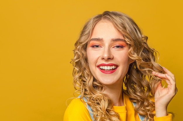 Mujer bonita con el pelo largo y rizado riendo sobre un fondo amarillo