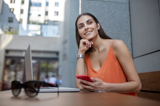 Mujer bonita de pelo oscuro con un smartphone mirando anticipado