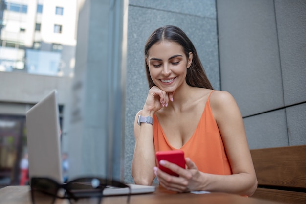 Mujer bonita de pelo oscuro con un teléfono inteligente en la mano sonriendo