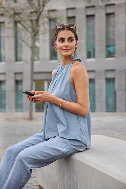 Mujer bonita pensativa en traje azul de moda sostiene teléfono móvil envía mensajes de texto usa smartphone