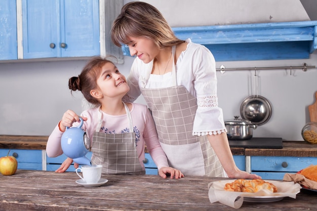 Mujer bonita y pequeña hija adorable de pie en la mesa en la cocina cocinan juntos