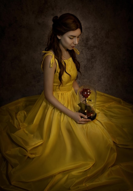 Mujer bonita en el primer plano de vestido amarillo con rosa roja en sus manosLa bella y la bestia cosplay