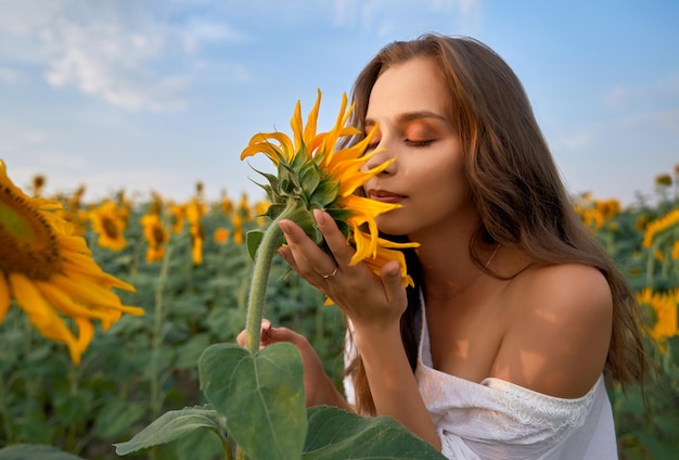 Mujer bonita que huele a girasol con los ojos cerrados en el campo