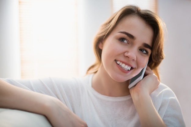 Mujer bonita que llama al teléfono en el sofá en la sala de estar