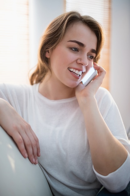 Mujer bonita que llama al teléfono en el sofá en la sala de estar