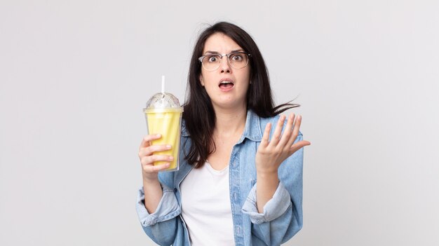 Foto mujer bonita que parece desesperada, frustrada y estresada y sosteniendo un batido de vainilla