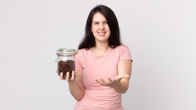 Mujer bonita que parece enojada, molesta y frustrada y sosteniendo una botella de granos de café