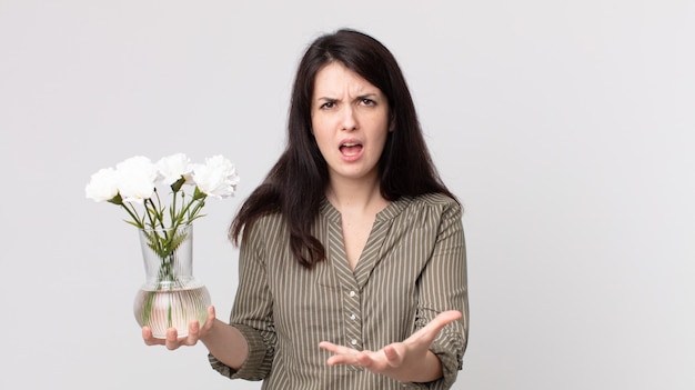 Mujer bonita que parece enojada, molesta y frustrada y sosteniendo flores decorativas. agente asistente con un auricular