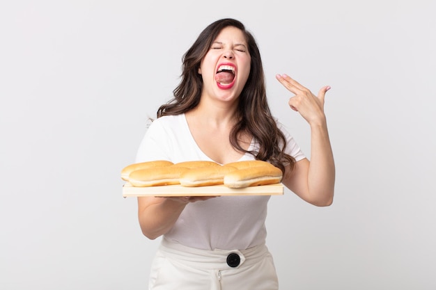 Mujer bonita que parece infeliz y estresada, gesto de suicidio haciendo un signo de pistola y sosteniendo una bandeja de rollo de pan