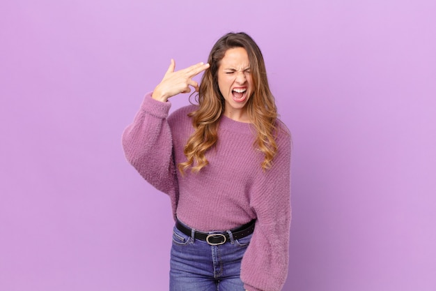 Mujer bonita que parece infeliz y estresada, gesto de suicidio haciendo signo de pistola